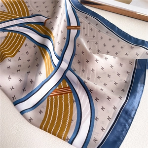 Close-up of silky 70x70cm square scarf featuring navy blue and yellow H-letter patterns