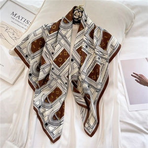 Close-up of silk square scarf with geometric patterns and camellia brooch on white shirt