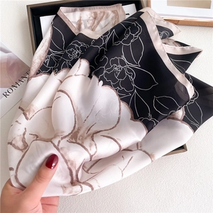 Elegant black and white camellia pattern satin scarf held to show silky drape and texture