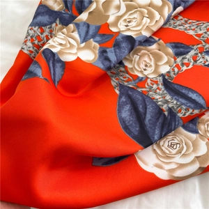 Macro detail of silk scarf showing orange camellia print and chain patterns on soft fabric