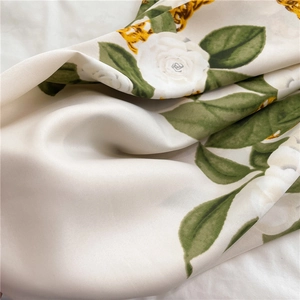 Macro detail of twill silk scarf showing white roses, green leaves, and golden chains
