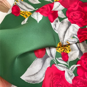 Close-up of matte silk-touch twill fabric with green base and red rose floral pattern