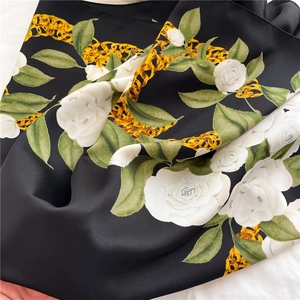 Close-up of matte silk scarf showing white camellia print and golden chain patterns