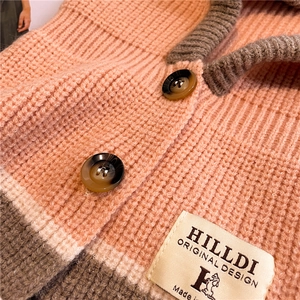 Close-up of thick pink knit texture with brown trim and amber-patterned buttons