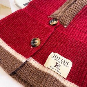 Close-up of chunky knit fabric in dark red with tortoiseshell button and brand tag