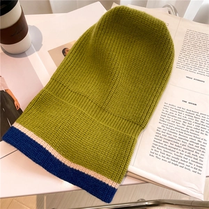 Detail of olive green knit balaclava with striped trim next to a coffee cup and magazine