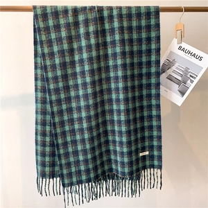 Detailed view of green and black checkered scarf with thick fringe on a metal rack