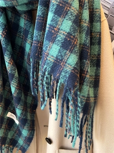 Detail of a thick plaid scarf with long tassels and green, blue, and orange checks