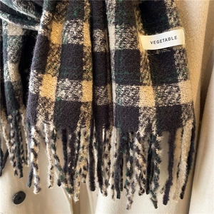 Close-up of green and black plaid cashmere scarf featuring soft tassels and brand tag
