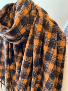 Detailed macro view of orange and black plaid scarf texture with soft fringe edges