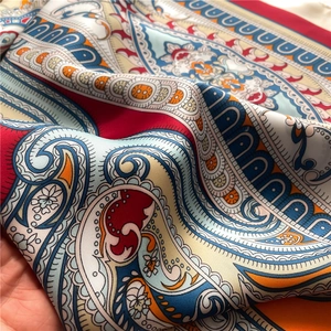 Detailed close-up of paisley pattern silk scarf with vibrant red borders and soft texture
