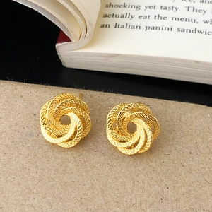 Détail des boucles d'oreilles torsadées dorées avec texture radiale sur papier
