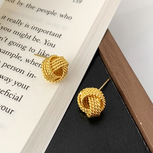 Gros plan détaillé de boucles d'oreilles nœuds dorés torsadés avec texture tissée sur livre