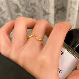 Detailed view of a minimalist gold wavy ring set against a soft aesthetic backdrop