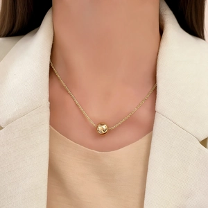 Collier minimaliste à pendentif boule dorée pour femme porté avec un blazer blanc chic