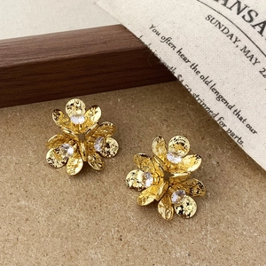 Makro-Detail von goldenen Blumenohrringen mit Kristallmitte auf Vintage-Stoff