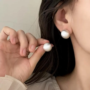 Macro detail of large matte silver spherical stud earrings with a brushed metal finish