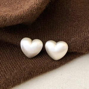 Macro shot of minimalist silver heart studs with a brushed matte metallic texture