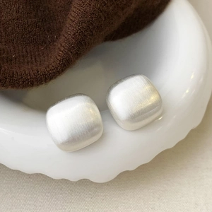 Detail of matte silver square studs with brushed metal texture on a ceramic tray