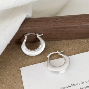 Detail of matte silver brushed hoop earrings on white linen with high texture