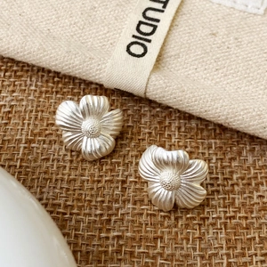 Macro detail of matte silver flower earrings with fine petal texture on rustic fabric