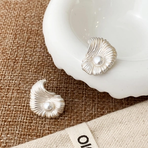 Detailed view of silver shell stud earrings with central white pearl on linen fabric