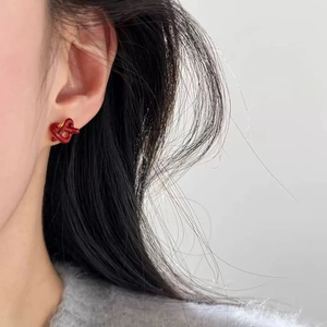 Detail view of stylish dark red knotted stud earrings with smooth enamel finish on model