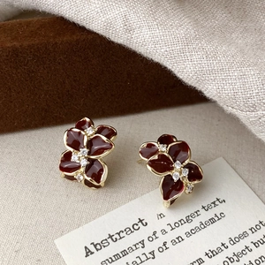 Detail of flower stud earrings featuring dark red enamel petals and zircon centers