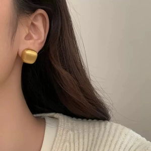 Close-up of minimalist gold square stud earring with matte brushed metal texture on ear