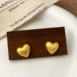 Detailed close-up of matte gold heart-shaped stud earrings with brushed metal texture