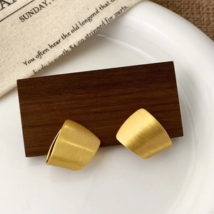 Detailed close-up of geometric brushed gold earrings on a rustic wood block