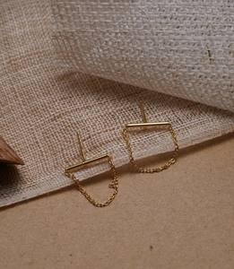 Macro detail of minimalist gold-plated link chain earrings with polished bar design