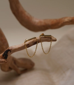 Detail of minimalist gold-plated chain earrings hanging on a natural wooden branch