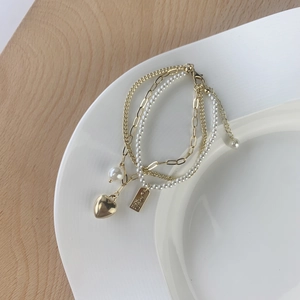 Elegant multi-layer gold bracelet with heart pendant and pearls on a white plate