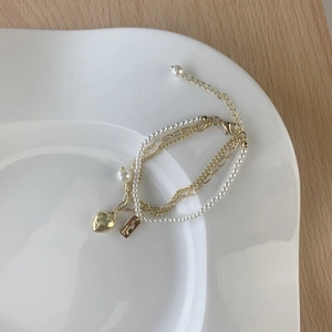 Multi-layer gold chain bracelet with white pearls and heart pendant on a white plate