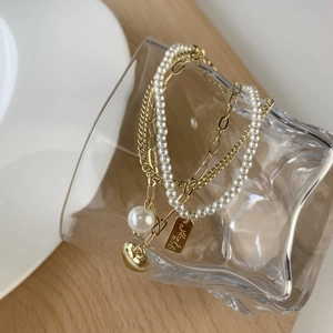 Layered gold heart bracelet with pearls and engraved metal plate on a glass
