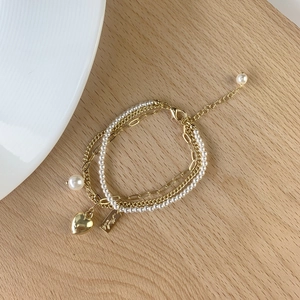 Detail view of multi-layer gold chain bracelet with pearls and heart pendant
