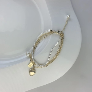 Detail shot of multi-layer gold plated bracelet with pearls and a heart charm
