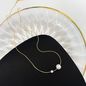 Close-up of gold-plated snake chain necklace with two elegant white pearls on a tray