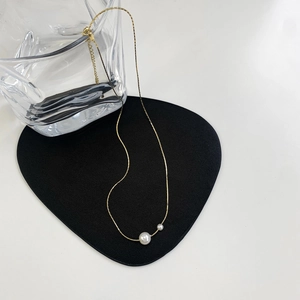 Detail of elegant gold-plated necklace with two white pearls on a minimalist background