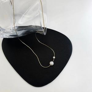 Detail of minimalist gold chain necklace with asymmetric double pearls on display