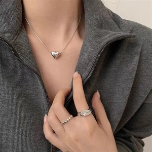 Dettaglio del ciondolo a cuore argento su catena a serpente con anelli indossati da modella