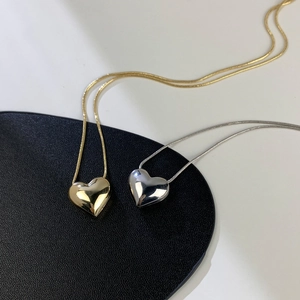 Dettaglio macro del ciondolo a cuore lucido e catena snake liscia in finiture oro e argento