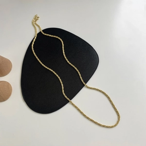 Close-up of a minimalist gold twisted rope chain necklace on a black textured cushion