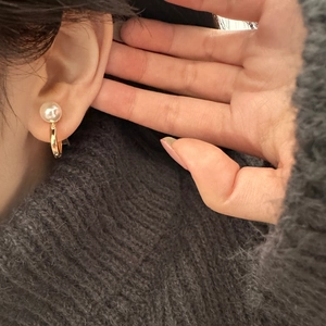 Close-up of elegant gold U-shaped earring featuring a glossy white pearl on a knit sweater
