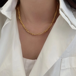 Close-up of a double-layered gold snake and bead chain necklace on a white collar