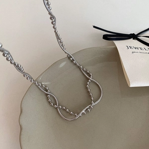 Detail of silver double layer necklace featuring bead and snake chains on ceramic plate