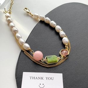 Detail of layered gold necklace with baroque pearls and multicolor gemstone charms