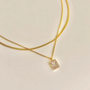 Detail of layered gold necklaces with herringbone chain and rectangular zircon pendant