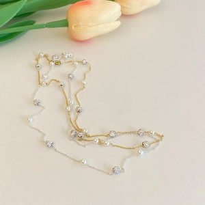 Détail du collier de perles baroques et zircons avec chaînes or et argent sur fond floral